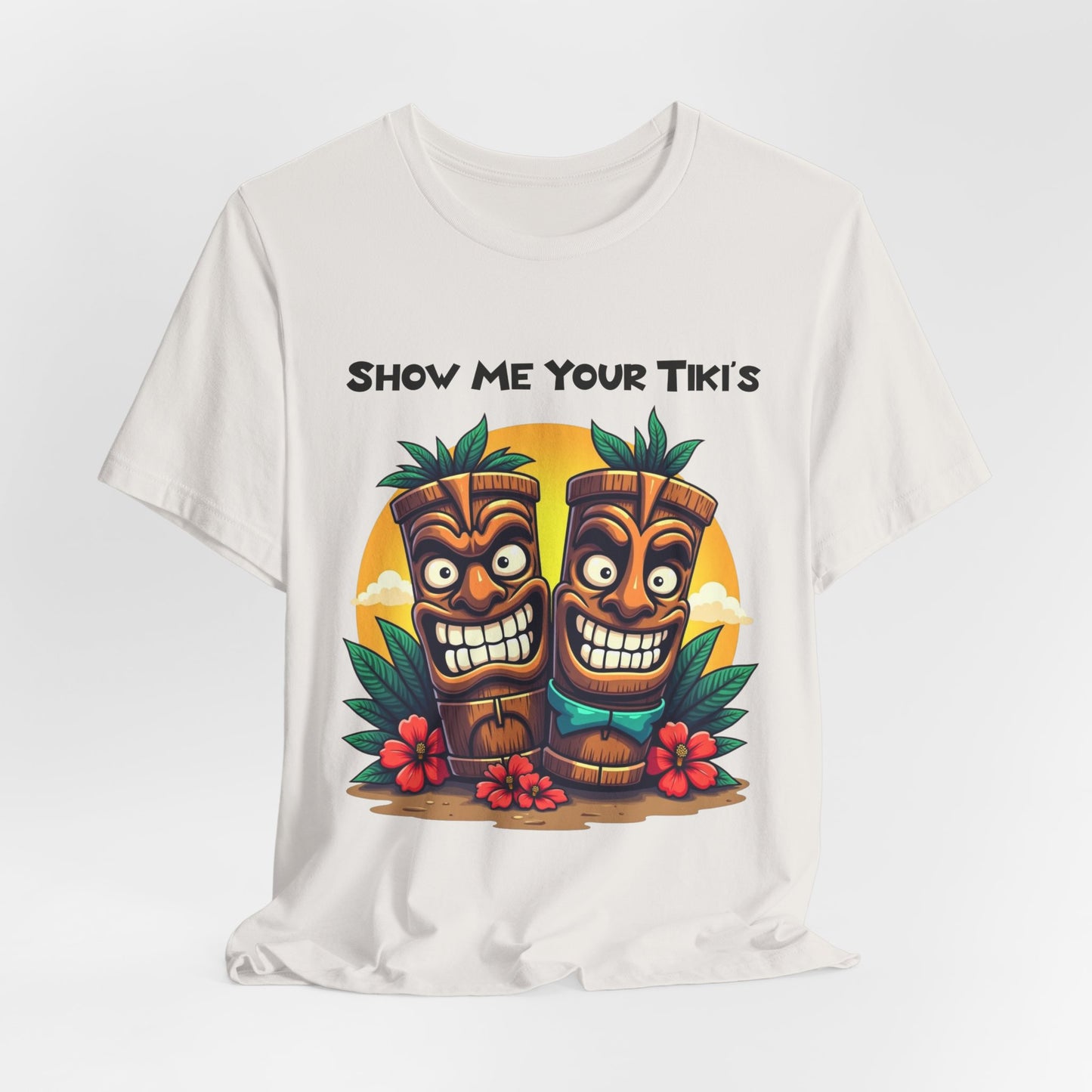 The Tiki Fun Unisex Jersey Short Sleeve Tiki T-Shirt features soft Airlume cotton and a tropical graphic with two colorful smiling tikis, leaves, red flowers, and Show Me Your Tiki’s text above them.