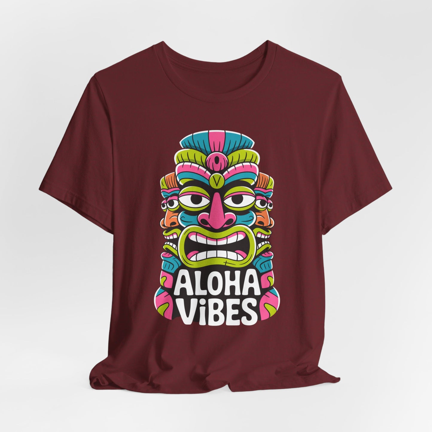 The Aloha Vibes Unisex Tiki T-Shirt - Fun Summer Graphic T-Shirt in maroon features a vibrant tiki mask above bold white text, offering adventurous and relaxed summer vibes. Displayed on a plain white background.