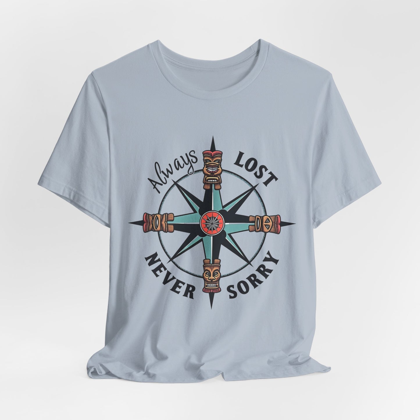 The Always Lost, Never Sorry Graphic Tee - Unisex Short Sleeve T-Shirt features a light blue color, compass design with tiki faces, and playful typography—perfect for those with an adventurous spirit.