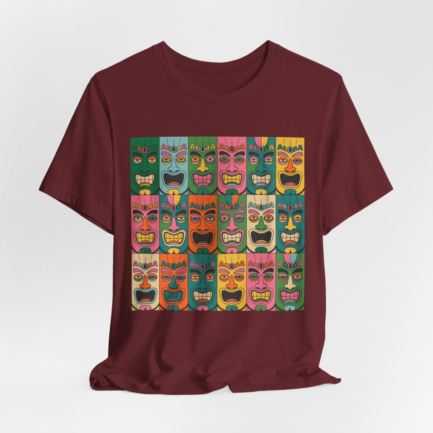 The Vibrant Tribal Mask Unisex Tiki T-Shirt showcases a maroon base with bold, colorful tiki mask graphics, combining eco-friendly manufacturing and unisex style in a striking grid design.