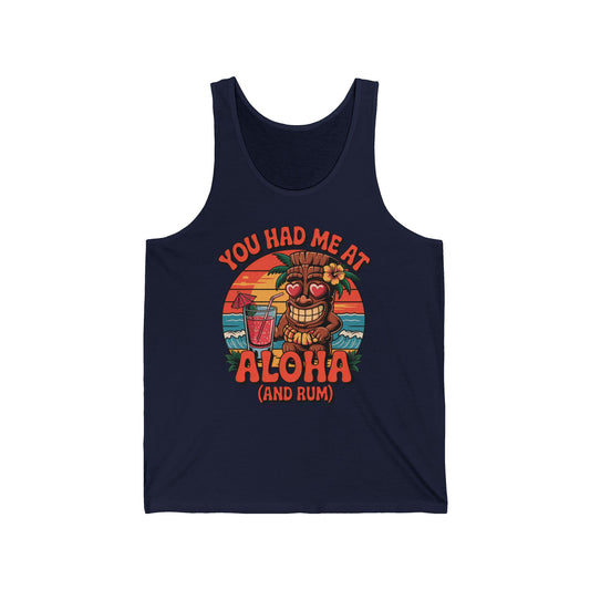 Aloha Tiki Tank Top: Unisex Jersey Tank in navy, features a cartoon tiki with heart-shaped sunglasses, tropical drink, palm trees at sunset, and You had me at Aloha (and rum) text. Embrace the tropical vibe!.