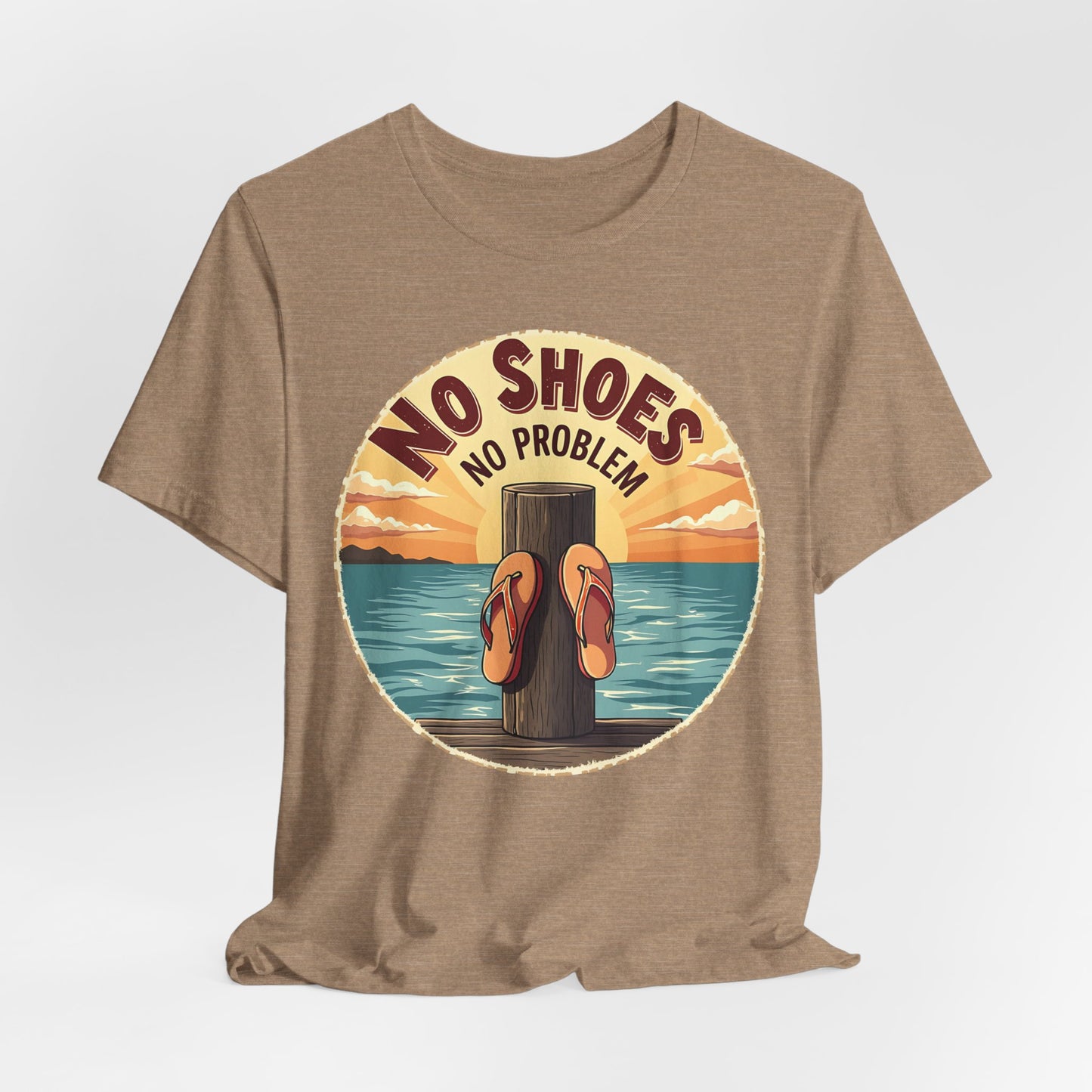 The Unisex No Shoes No Problem Graphic Tee is a casual beach vibe shirt featuring flip-flops on a pier post with a sunset over water and bold No Shoes, No Problem text—perfect for anyone embracing the coastal lifestyle.