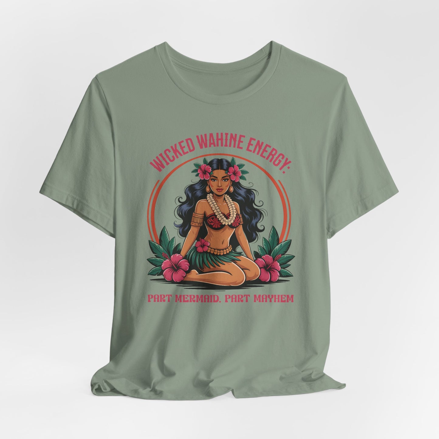 The Wicked Wahine Energy Unisex Tee—Part Mermaid, Part Mayhem—features a sage green jersey and an illustrated woman with long dark hair, flower crown, and grass skirt. “WICKED WAHINE ENERGY: PART MERMAID, PART MAYHEM” is printed on the front.