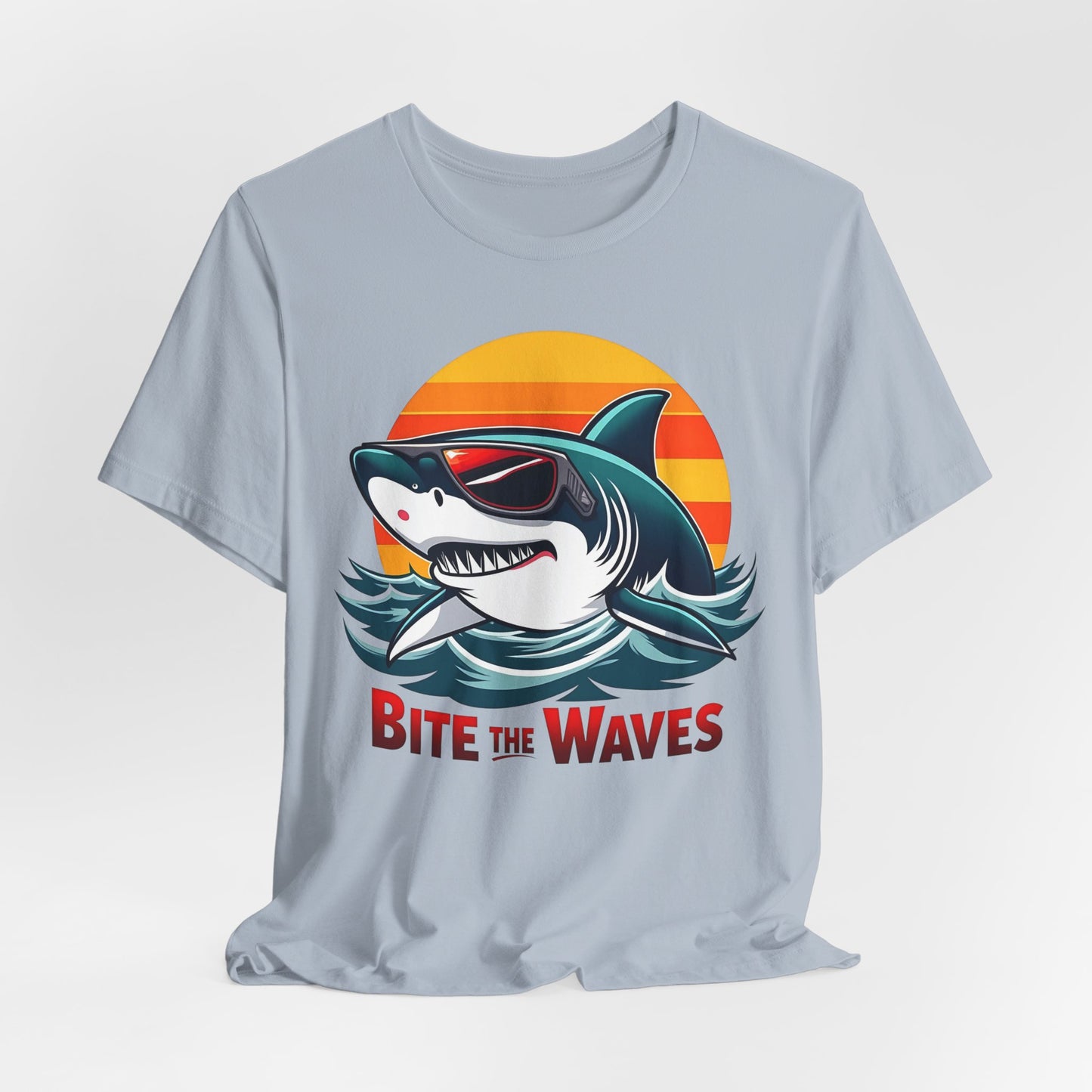 The Bite the Waves Shark T-Shirt is a light gray unisex jersey featuring a cartoon shark in sunglasses, ocean waves, and a retro sunset. Bold red BITE THE WAVES text makes it perfect for beach vacations.