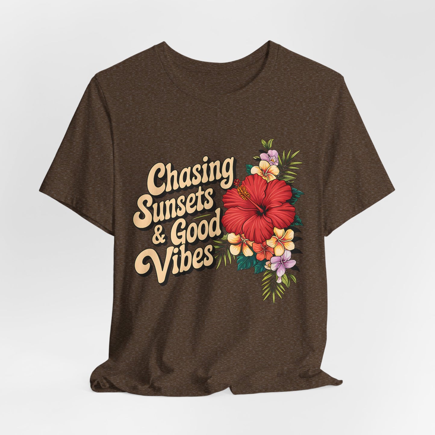 The Chasing Sunsets & Good Vibes Tee is a unisex jersey shirt featuring bold cream lettering and a vibrant floral design—large red hibiscus with purple, yellow, and white flowers—perfect for summer adventures with carefree spirit.