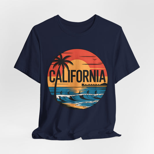 The California Sunset Graphic T-Shirt is a navy blue unisex tee with a colorful sunset, palm trees, waves, surfers, and CALIFORNIA—made from breathable cotton for summer style.