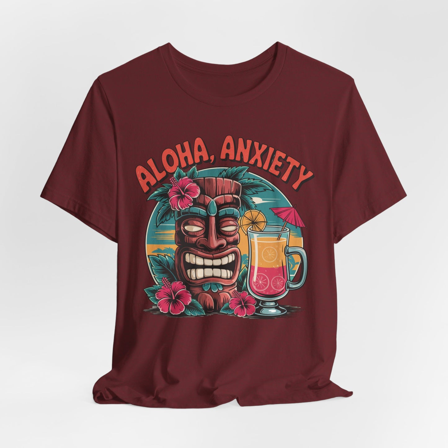 The Aloha Anxiety Unisex Short Sleeve Tiki T-Shirt in burgundy features a tiki mask, tropical flowers, and a fruity drink beneath Aloha Anxiety, all on soft Airlume cotton for relaxed island vibes and comfort.