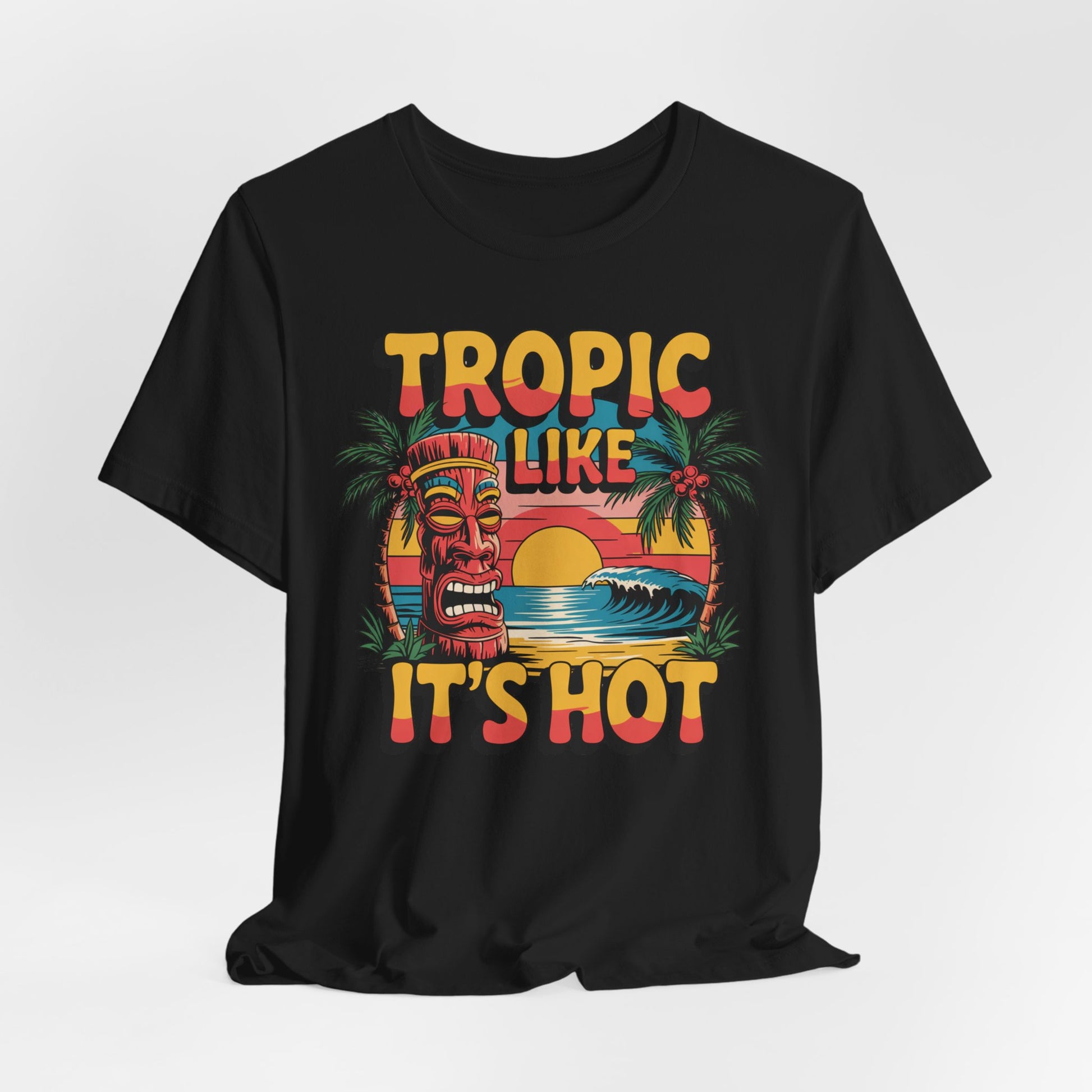 The Tropic Like Its Hot Unisex Tiki T-Shirt features a vibrant tiki face, palm trees, waves, and sunset with bold TROPIC LIKE ITS HOT text—perfect for summer festivals, beach days, or vacation vibes.