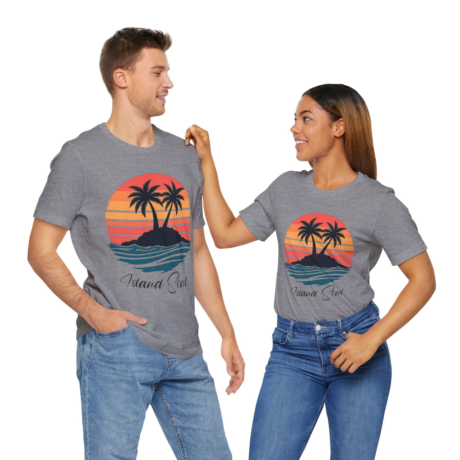 A man and woman in blue jeans relax together in matching Island Soul Unisex T-Shirts—Retro Sunset Tee with palm trees—smiling and capturing laid-back island vibes against a clean white background.