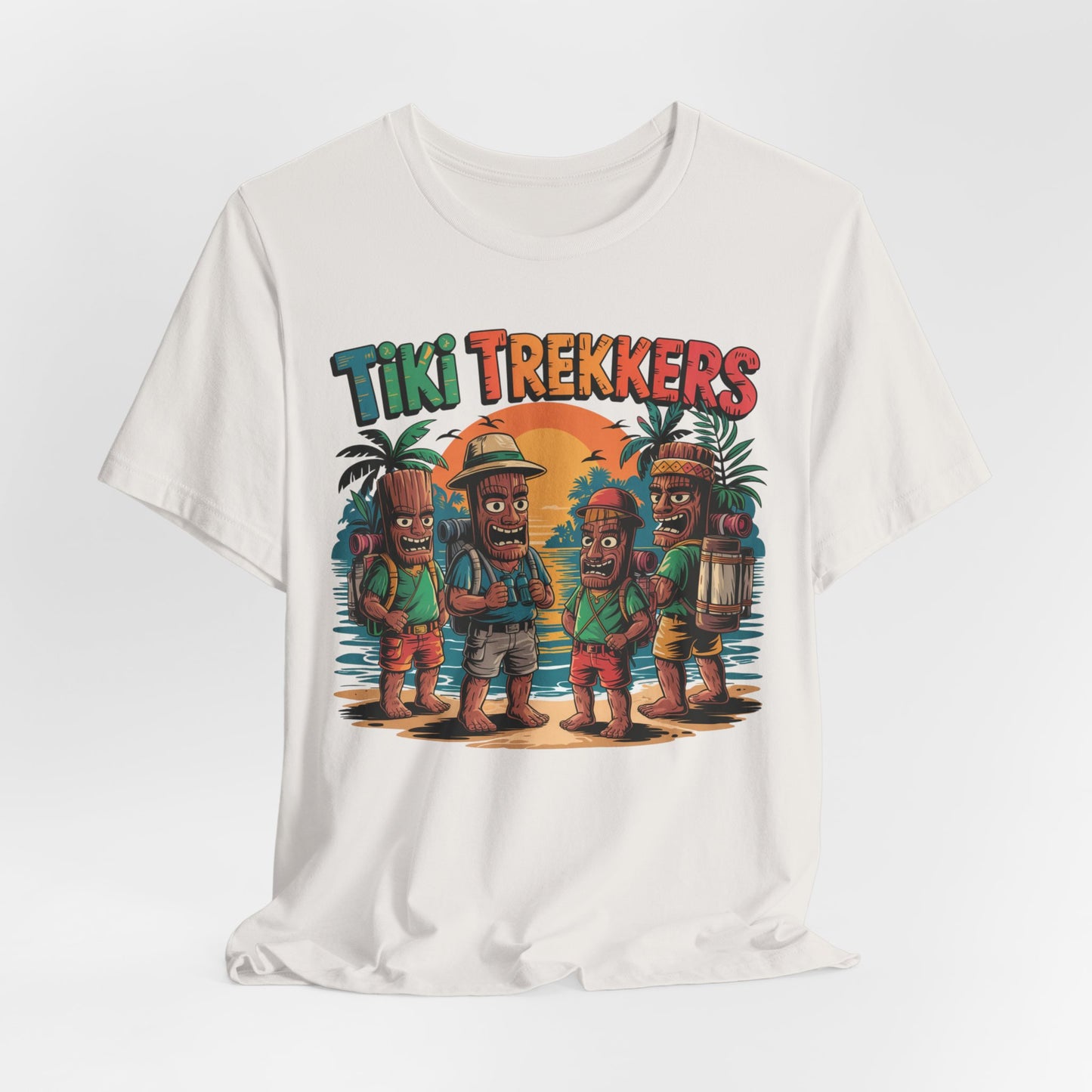 The Tiki Trekkers Graphic Tiki T-Shirt is a white unisex jersey featuring four tiki characters as trekkers with tropical trees and a sunset, topped by bold Tiki Trekkers text—perfect for adventure lovers.