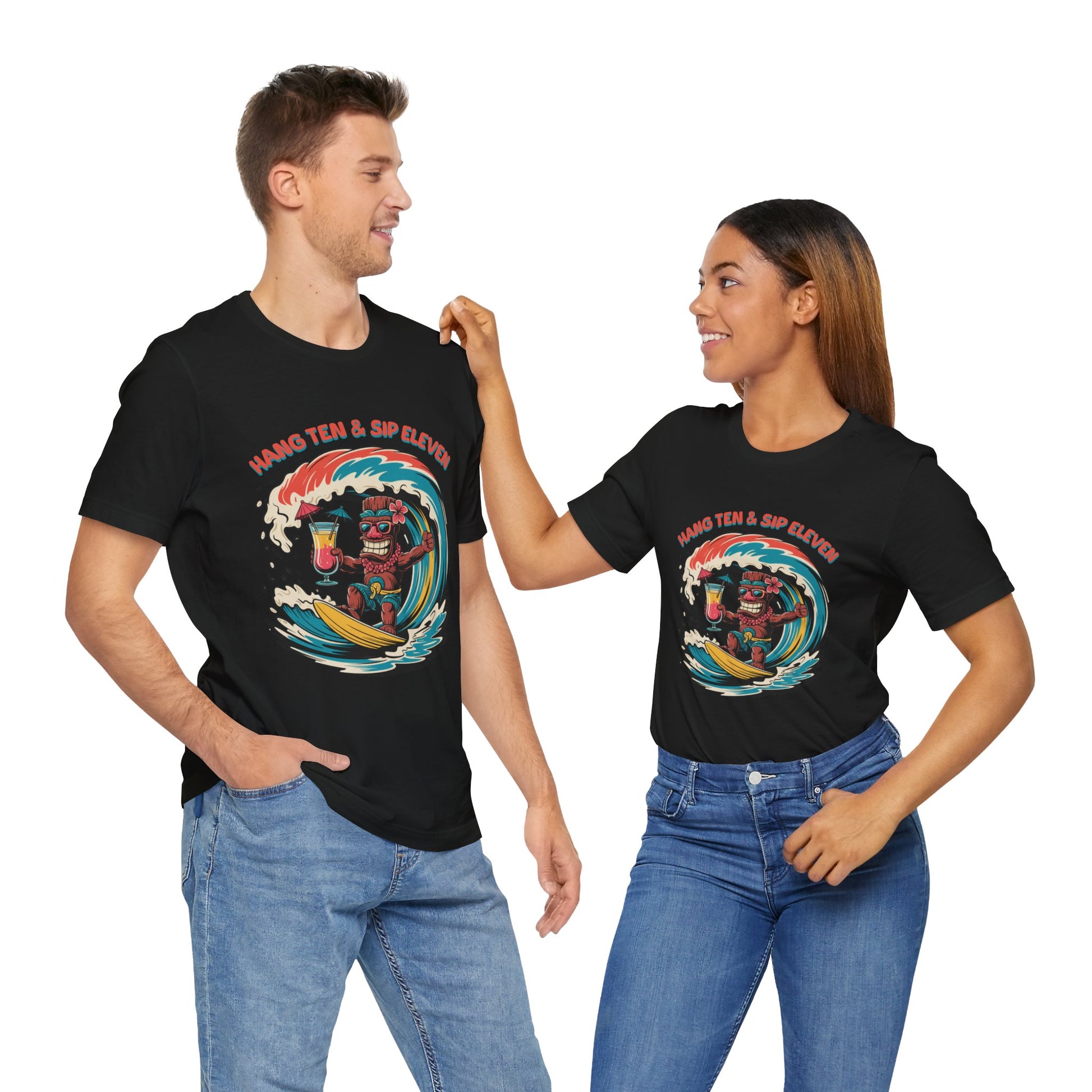 A man and woman smile at each other in matching Surf Vibe Tiki Unisex Jersey T-Shirts, featuring a colorful surf-inspired Hang Ten & Sip Eleven design. Both pose casually in jeans.