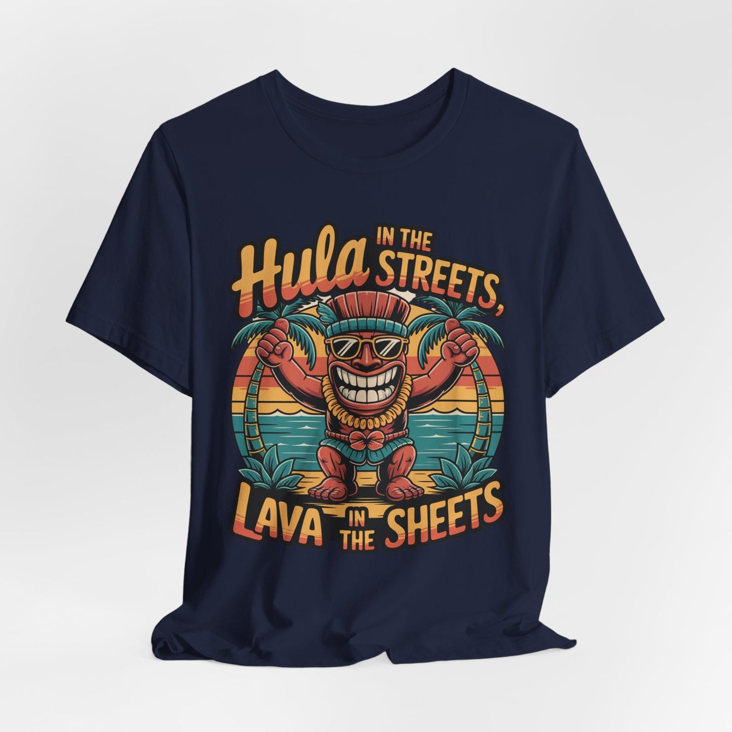 The Hula in the Streets Short Sleeve Tiki T-Shirt features a smiling tiki with sunglasses and grass skirt between palm trees. The text reads: Hula in the streets, lava in the sheets. Perfect for summer celebrations and tropical vibes.