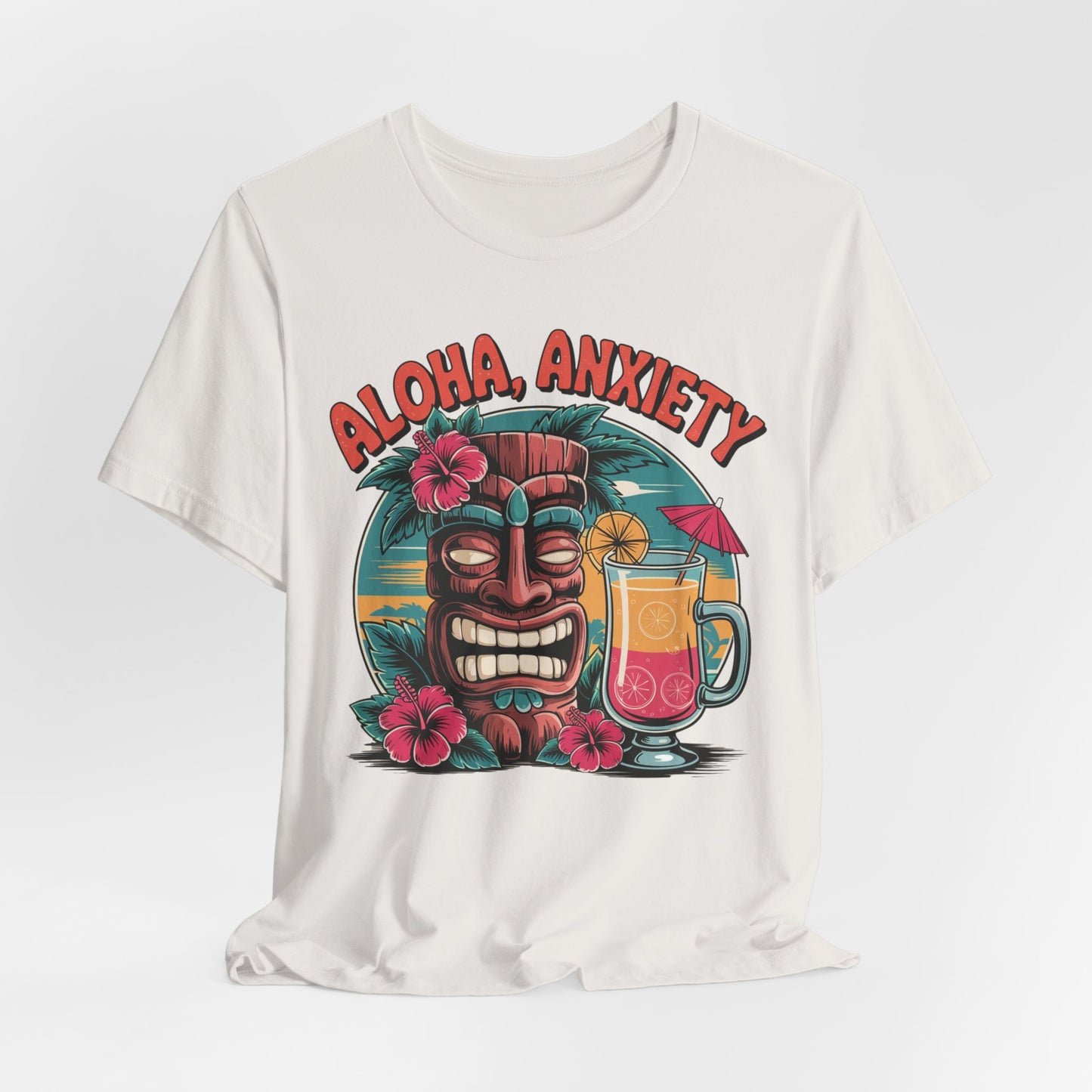 The Aloha Anxiety Unisex Short Sleeve Tiki T-Shirt features a grinning tiki mask, pink hibiscus, and a tropical drink on soft Airlume cotton, with “ALOHA ANXIETY” above the vibrant island-inspired design.