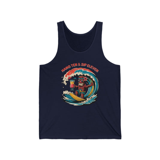 The Hang Ten and Sip Eleven- Tiki Tank Top is a navy blue unisex jersey made from soft Airlume combed cotton, featuring a high-quality print of a surfing tiki with a drink and bold HANG TEN & SIP ELEVEN text above.