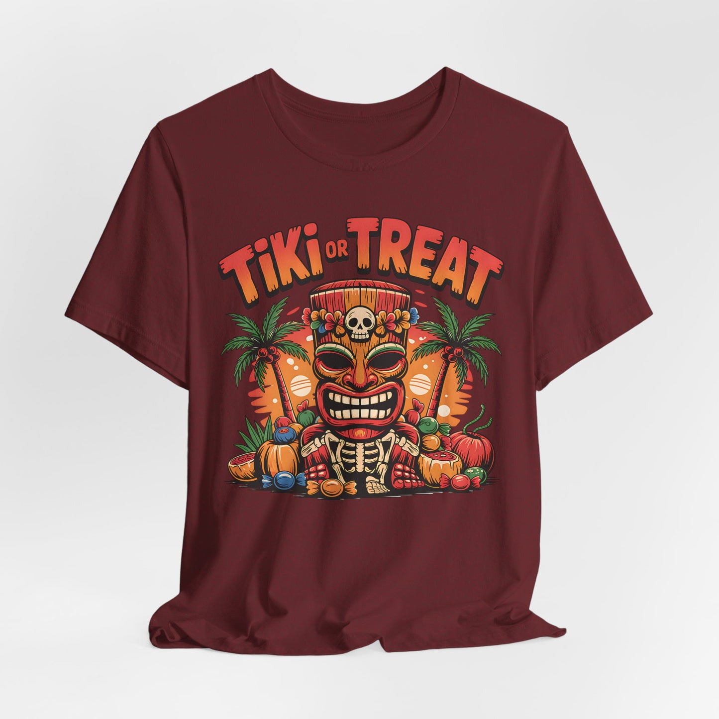 The Tiki or Treat Halloween Tiki T-Shirt - Unisex Jersey Short Sleeve Tee features a maroon design with a colorful tiki mask, skull crown, palm trees, pumpkins, candy, and Tiki or Treat—ideal for a festive tropical vibe.