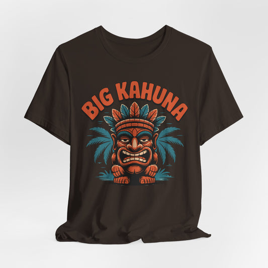 The Tiki T-Shirt - Big Kahuna Tropical Vibe Unisex T-Shirt is a black jersey tee with colorful cartoon tiki face graphics, a feathered headdress, palm leaves, and BIG KAHUNA in bold orange lettering above the design.