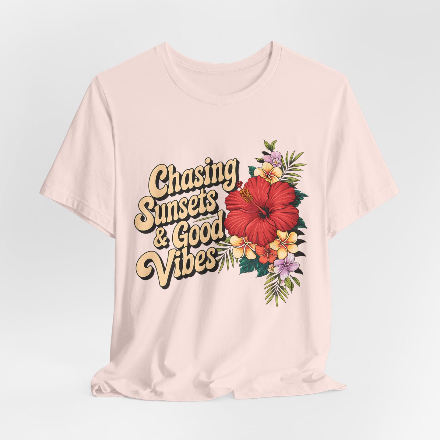 The Chasing Sunsets & Good Vibes Tee is a light beige unisex jersey shirt for summer adventures, featuring retro lettering and a vibrant floral design with a large red hibiscus and colorful flowers on the front.