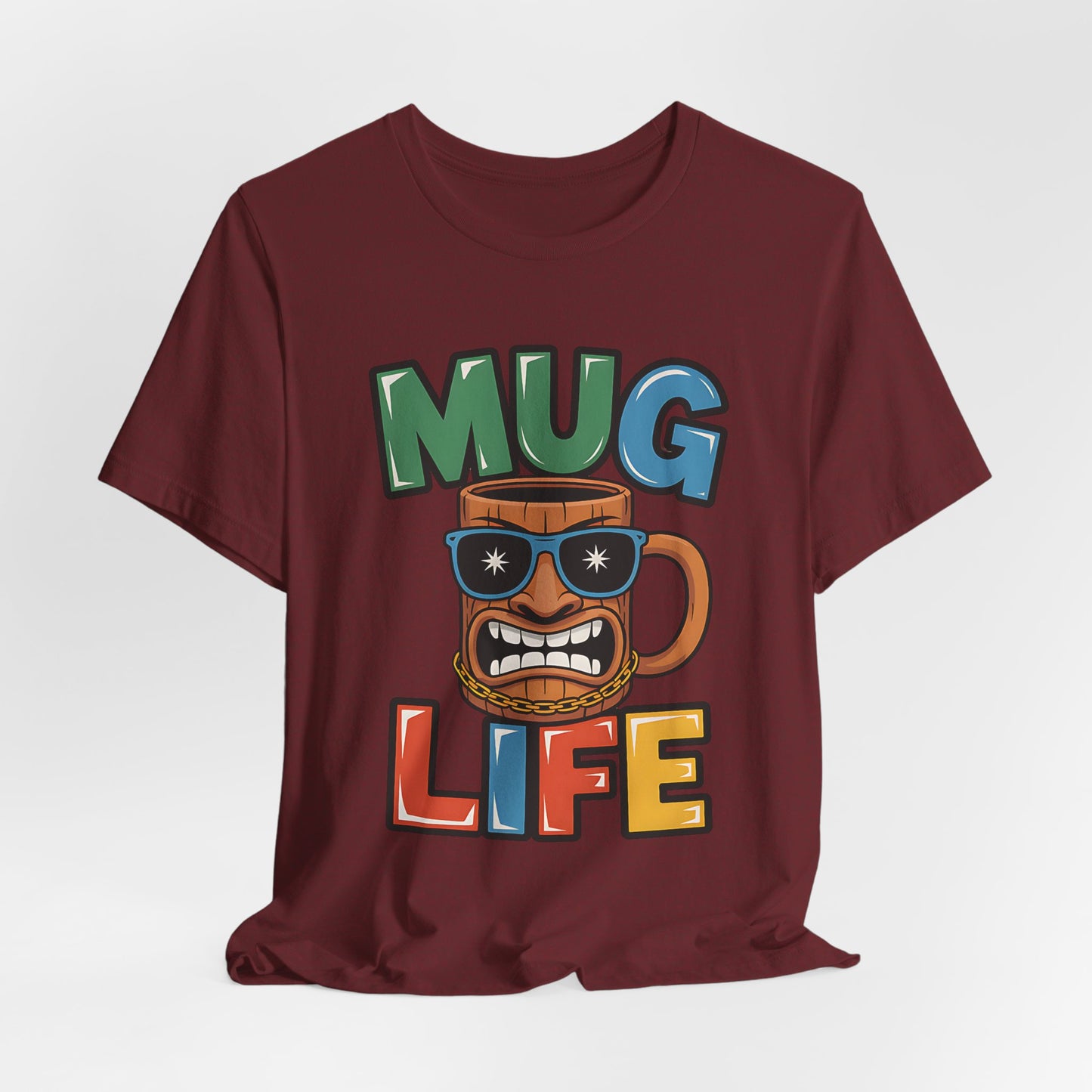 The Mug Life Graphic Tiki T-Shirt is a maroon unisex jersey tee featuring a cartoon mug with sunglasses, gold chain, and a grin, plus bold MUG LIFE text—ideal for coffee lovers with attitude.