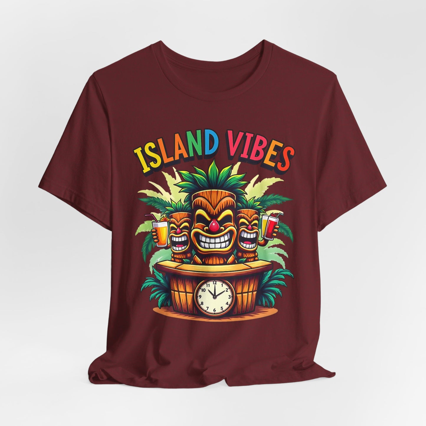 The Island Vibes Tiki T-Shirt is a maroon unisex relaxed fit shirt with three tiki faces, tropical leaves, drinks, a clock, and “ISLAND VIBES” in rainbow letters—ideal for beach lovers and anyone who loves the island lifestyle.