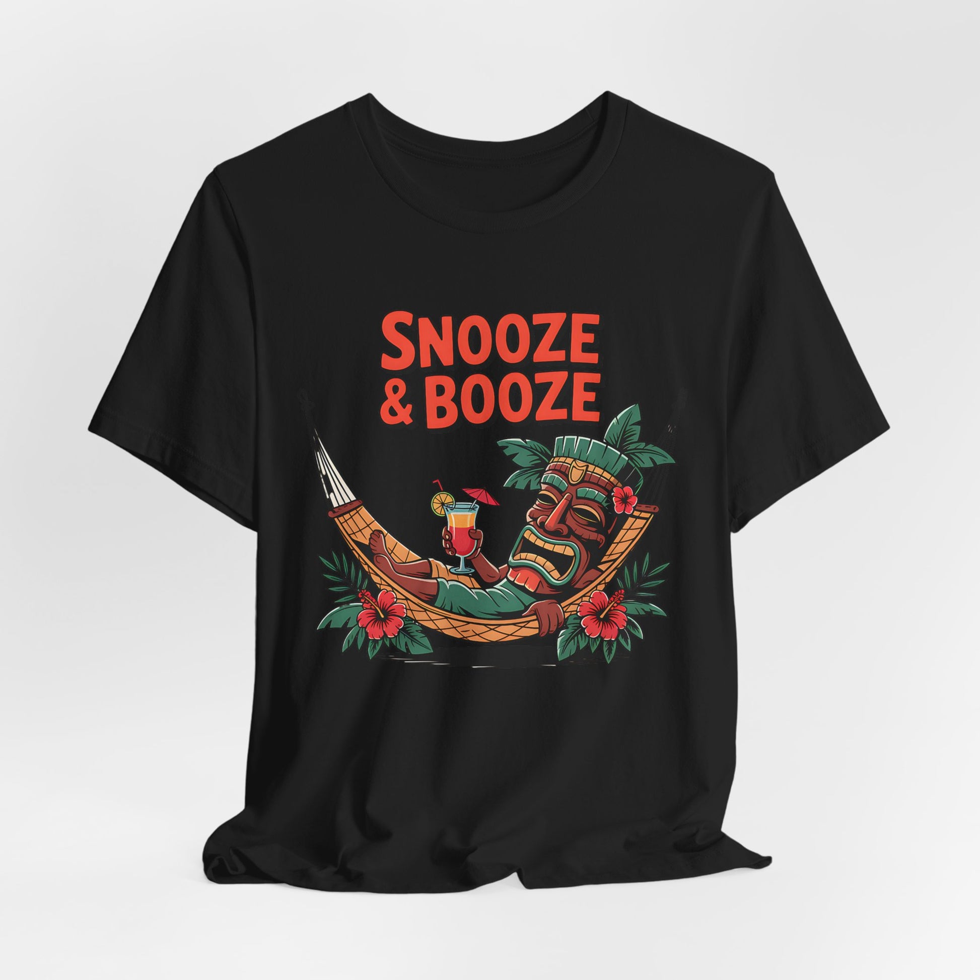 The Snooze & Booze Unisex Jersey Tiki T-Shirt brings tropical vacation vibes with a tiki statue lounging in a hammock, cocktail in hand, amidst leaves and red flowers. Bold Snooze & Booze text adds the perfect finishing touch.