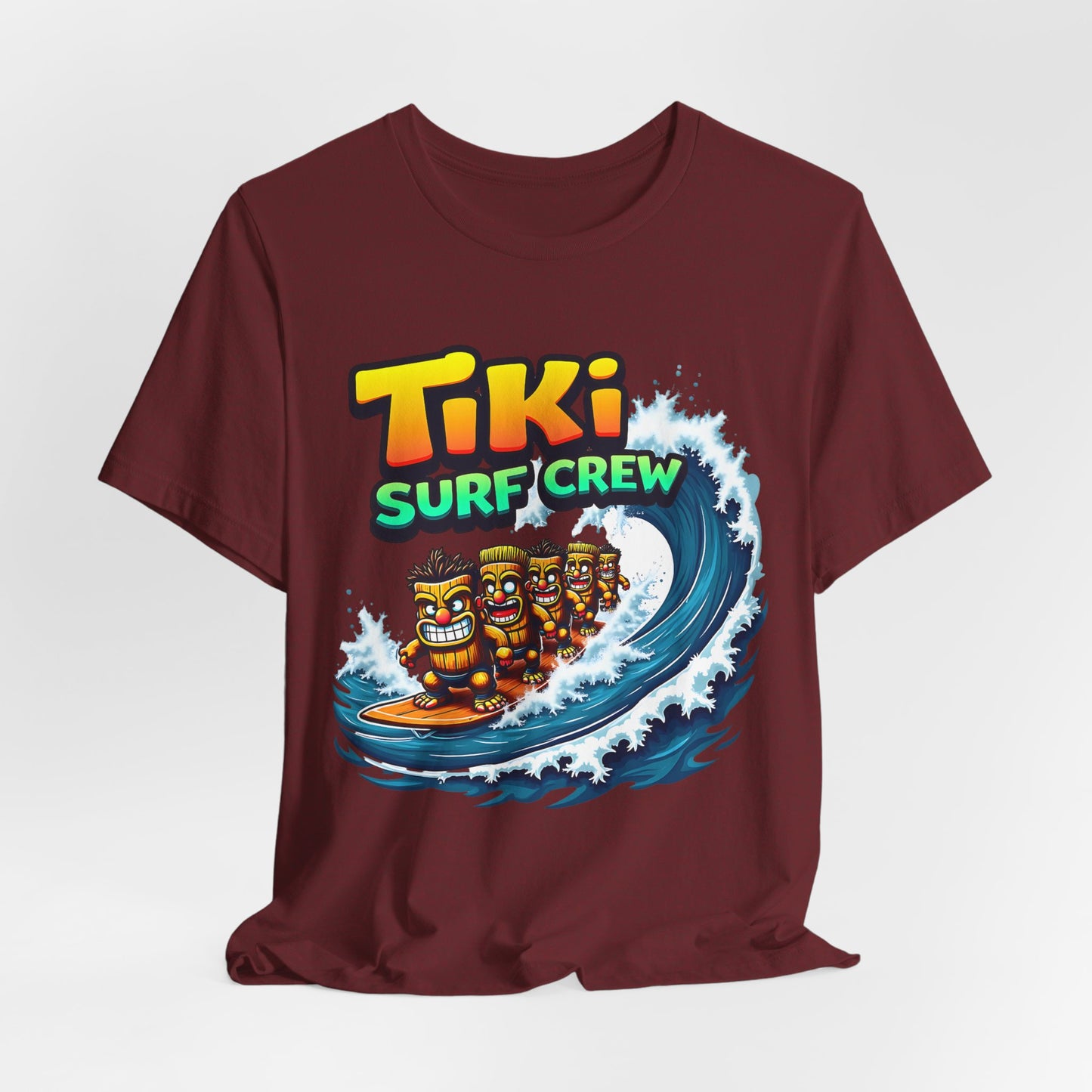 The Tiki Surf Crew Graphic Tiki T-Shirt is a fun unisex jersey short sleeve shirt featuring cartoon tiki figures surfing a blue wave with bold, colorful text—perfect for surf lovers and beach enthusiasts.