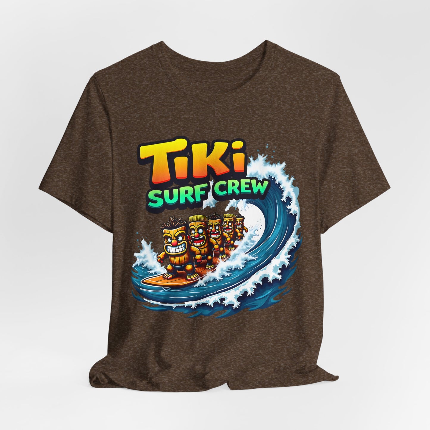 The Tiki Surf Crew Graphic Tiki T-Shirt is a fun unisex jersey short sleeve shirt featuring three cartoon tikis surfing a blue wave with vibrant Tiki Surf Crew text—ideal for surf lovers and beach fans.