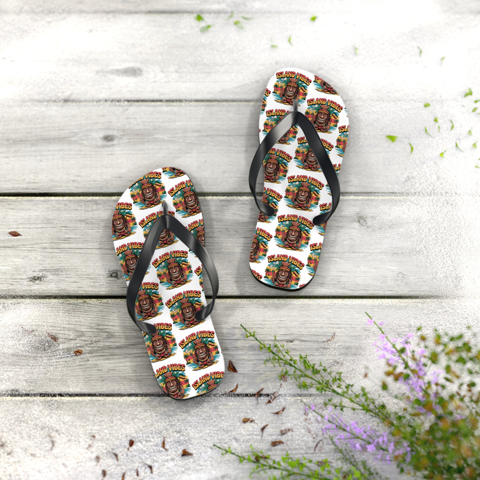 Island Vibes Tiki Flip Flops – Colorful Casual Footwear for Summer Fun with vibrant cartoon faces and text, displayed on a light wooden surface with leaves and purple flowers; ideal for beach lovers or summer vacations.