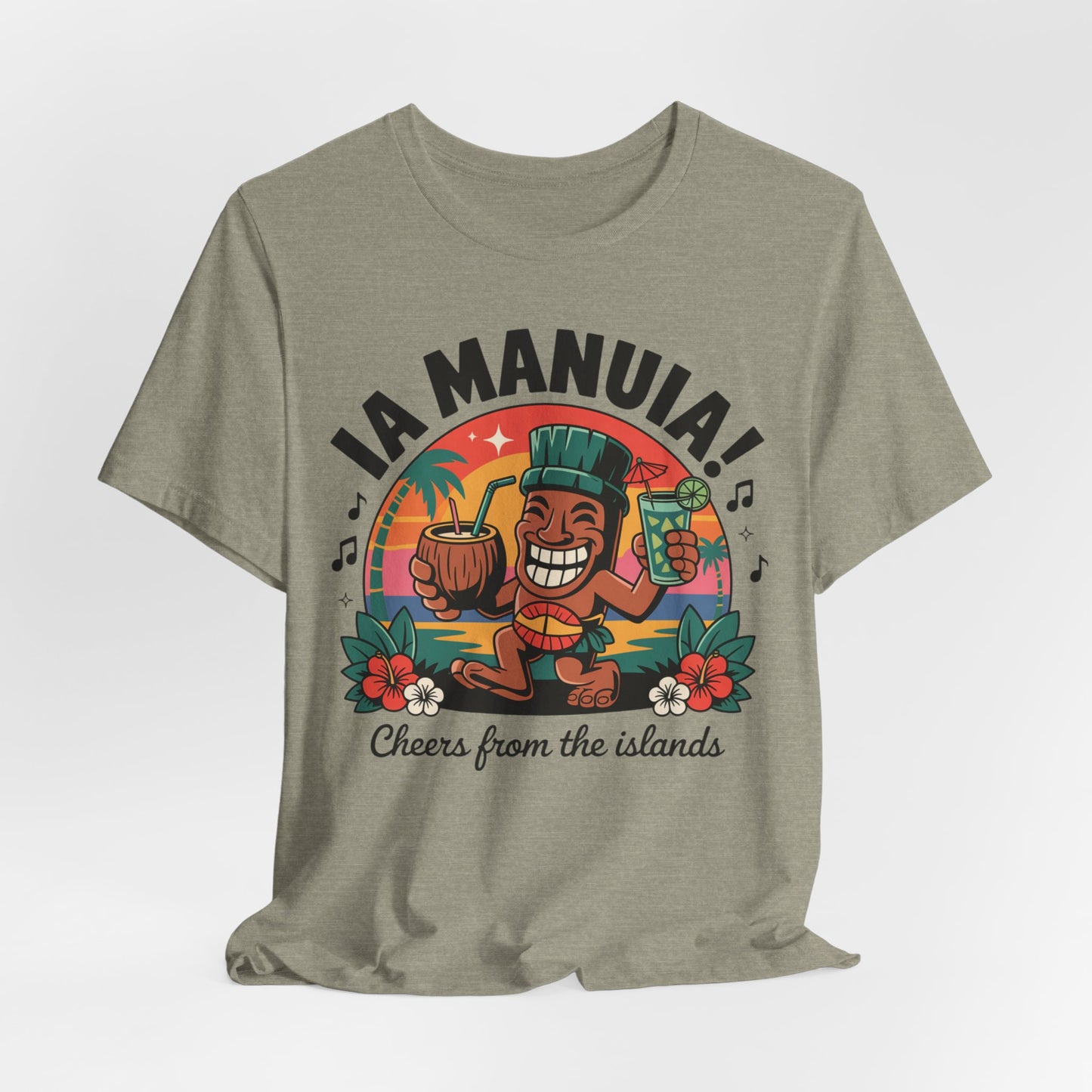 The IA MANUIA! Island Vibes Unisex Jersey Tiki T-Shirt, in light olive breathable cotton, features a smiling cartoon tiki with tropical drinks, palm trees, flowers, and IA MANUIA! Cheers from the islands—ideal for tropical events.