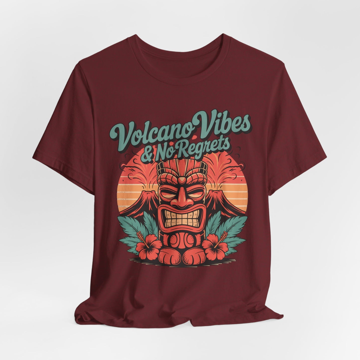 The Volcano Vibes and No Regrets Unisex Tiki T-Shirt is a maroon short sleeve tee with a stylized tiki face, tropical leaves, hibiscus flowers, and bold retro lettering—perfect for summer adventures and stylish comfort.