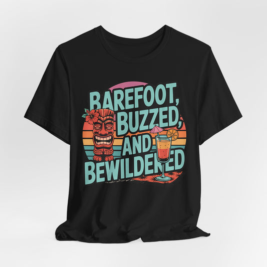 The Tropical Vibes Tiki T-Shirt features Barefoot, Buzzed, and Bewildered text, a smiling tiki statue, cocktail with orange slice, and retro sunset stripes—perfect for unisex summer celebrations.
