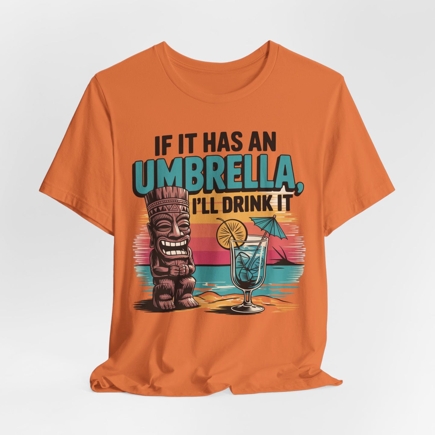 The Tropical Fun Tiki T-Shirt features a tiki figure, tropical cocktail with an umbrella, and the text If It Has an Umbrella, Ill Drink It on an orange tee with a beach sunset background for ultimate tropical vibes.