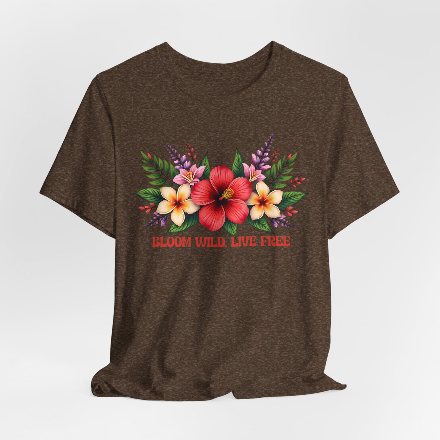 The Bloom Wild, Live Free Floral Tee is a brown unisex jersey short sleeve shirt with a vibrant floral print and “BLOOM WILD, LIVE FREE” in red below the tropical flowers and green leaves.