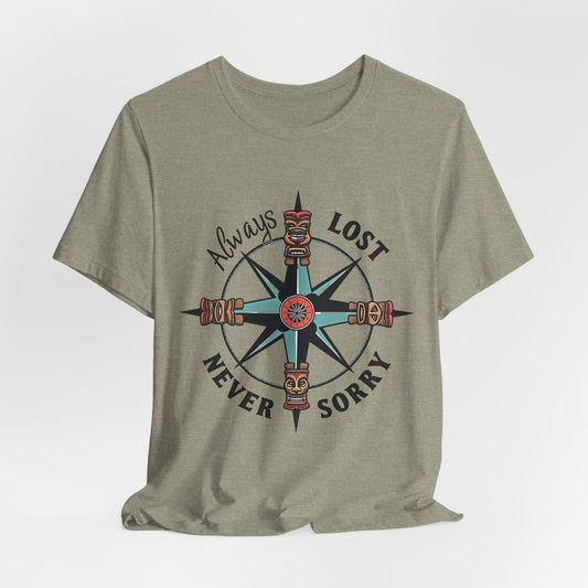 The Always Lost, Never Sorry Graphic Tee is a light olive green unisex short sleeve shirt featuring a compass with tiki faces and the motto Always Lost Never Sorry—perfect for those with an adventurous spirit.