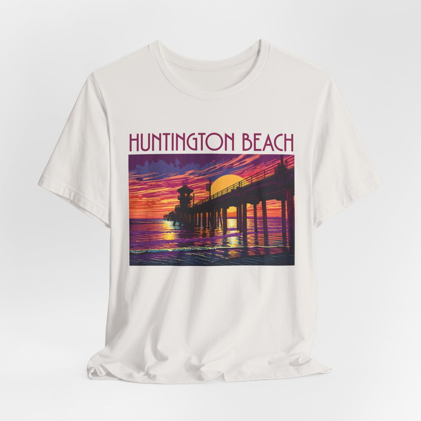 The Huntington Beach Sunset T-Shirt - Unisex Jersey Short Sleeve features a vibrant pier-at-sunset graphic with HUNTINGTON BEACH in bold red, celebrating iconic beach culture.
