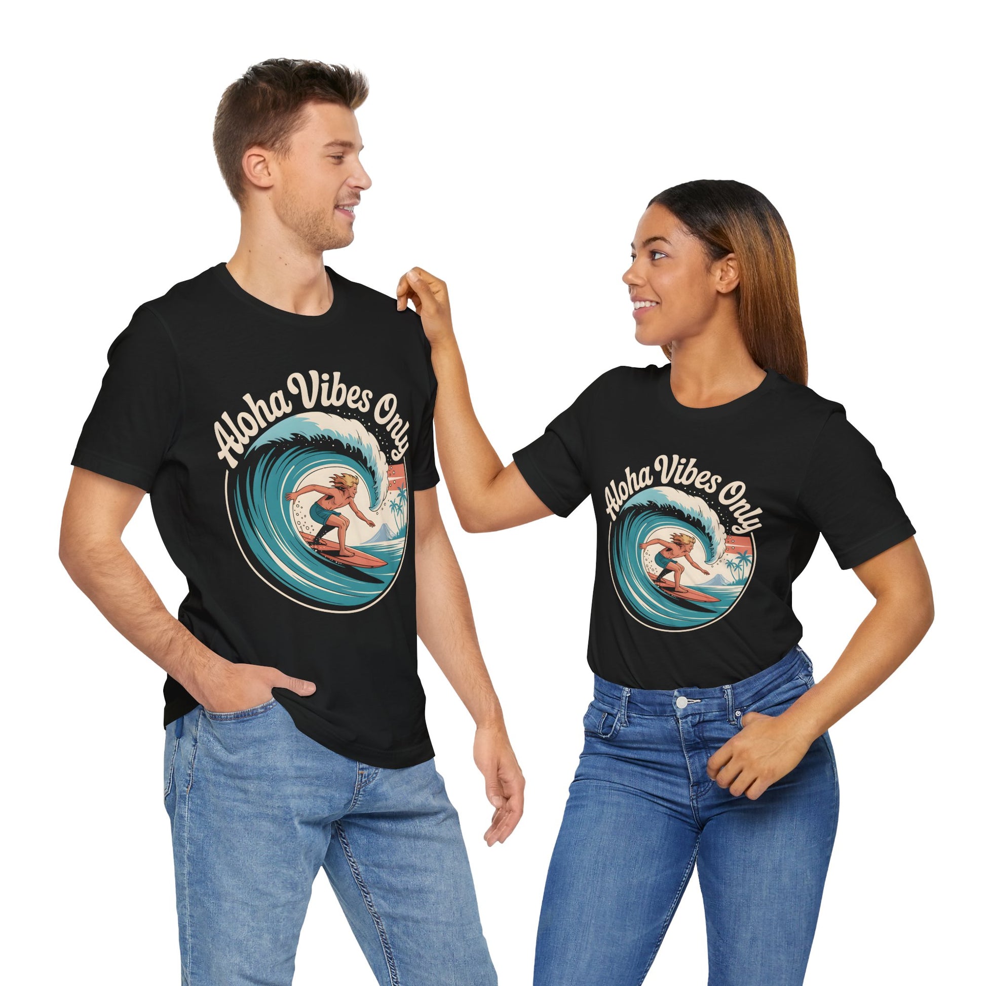 A beach-loving couple smiles at each other in matching Aloha Vibes Only Surf T-Shirts with a surfing graphic, one hand in their pockets, as she touches his shoulder—perfectly capturing the laid-back surf spirit.
