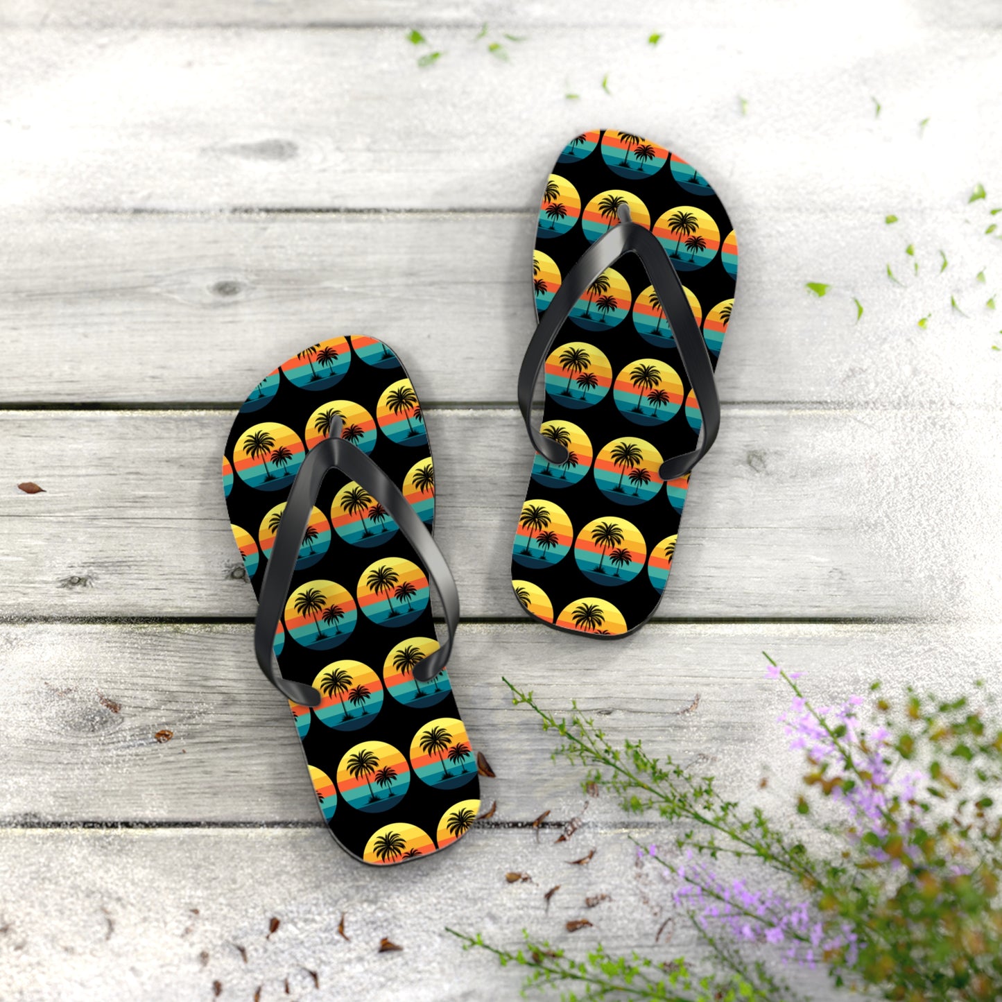 The Tropical Sunset Flip Flops - Summer Vibes with Palm Trees feature a vibrant sunset and palm tree design, resting on weathered wood, perfect for beach lovers. Scattered leaves and purple flowers accent the scene.