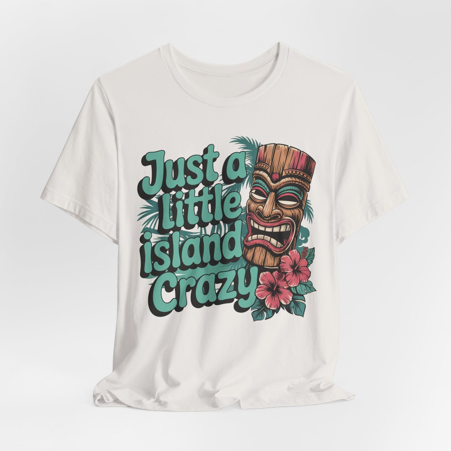 The Tiki Island Crazy Unisex Tiki T-Shirt features a vibrant tiki mask, lush tropical details, pink hibiscus flowers, and bold Just a little island crazy text—perfect for fun island culture vibes.
