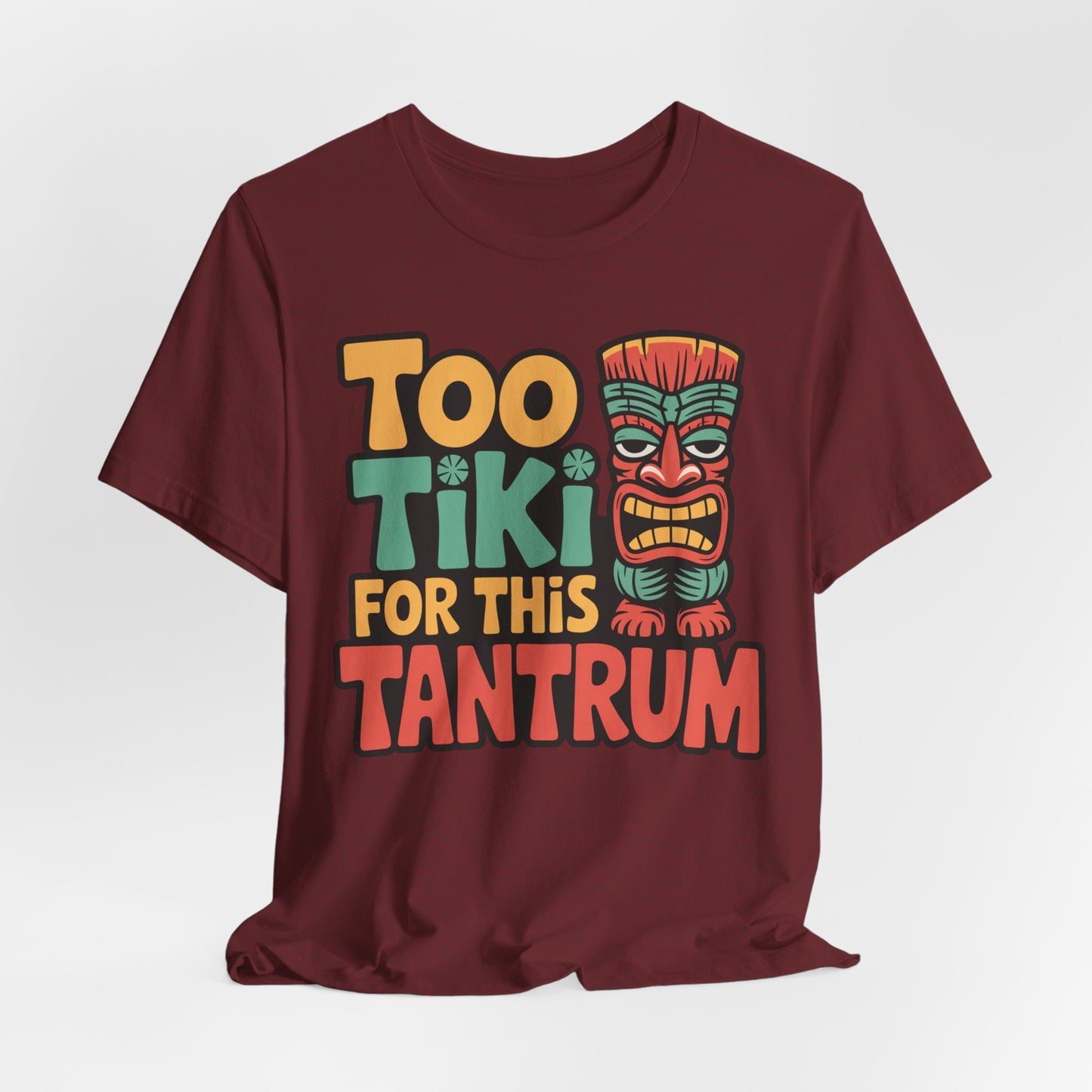 The Tiki Tantrum T-Shirt is a maroon unisex jersey tee featuring Too Tiki For This Tantrum in colorful text and a cartoon tiki mask in green, red, and yellow. Made from breathable fabric, its perfect for tropical vibes and celebrations. Plain white background.