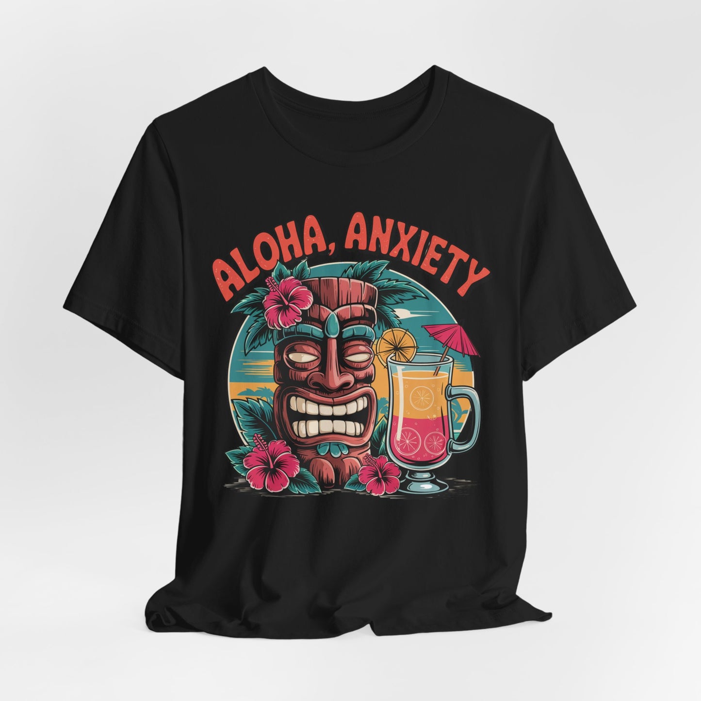 The Aloha Anxiety Unisex Short Sleeve Tiki T-Shirt features a grinning tiki mask with pink flowers, a sunset, and tropical drink. Aloha Anxiety appears in bold red above the vibrant design on soft Airlume cotton for a relaxed island vibe.