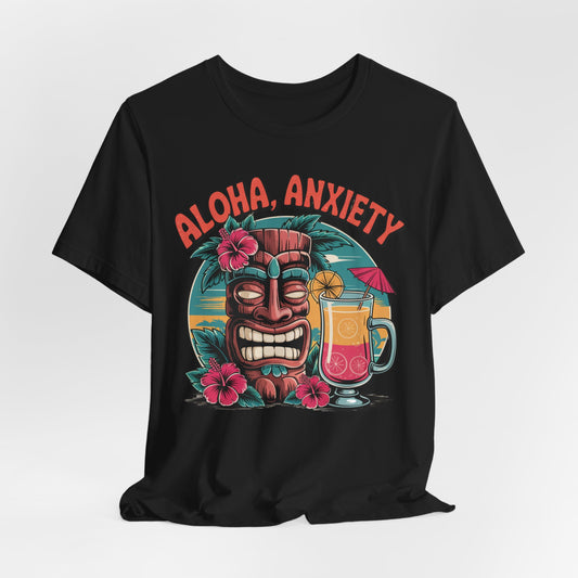 The Aloha Anxiety Unisex Short Sleeve Tiki T-Shirt features a grinning tiki mask with pink flowers, a sunset, and tropical drink. Aloha Anxiety appears in bold red above the vibrant design on soft Airlume cotton for a relaxed island vibe.