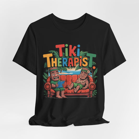 The Tiki Therapist Unisex Tiki T-Shirt is a fun Hawaiian graphic tee for beach lovers, featuring two smiling tiki figures on a red couch with Tiki Therapist above, tropical leaves accents, and made from breathable cotton for all-day comfort.