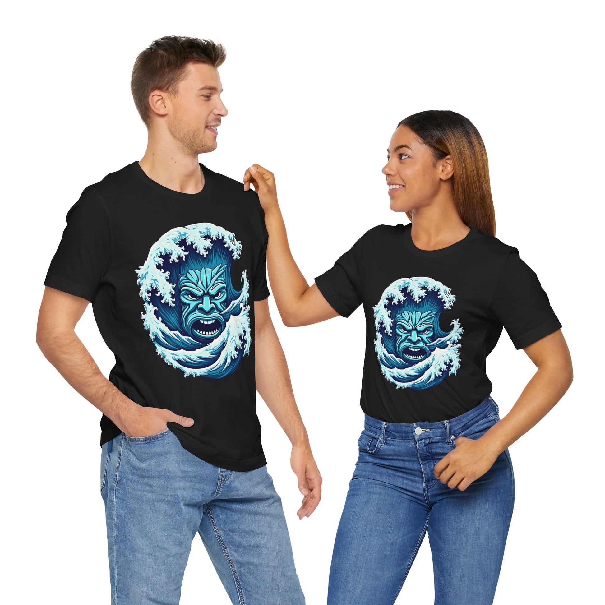 A man and woman, both beach lovers, wear matching black Ocean Wave Tiki- Adventure Vibes Unisex Jersey T-Shirts featuring a blue wave and fierce face design. Smiling in blue jeans, they pose against a white backdrop.