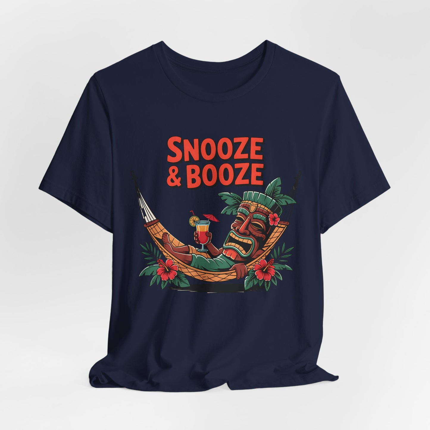 The Snooze & Booze Unisex Jersey Tiki T-Shirt features a colorful tiki mask lounging with a cocktail, tropical leaves, and flowers on navy blue—plus bold red SNOOZE & BOOZE text for ultimate vacation vibes in your casual style.