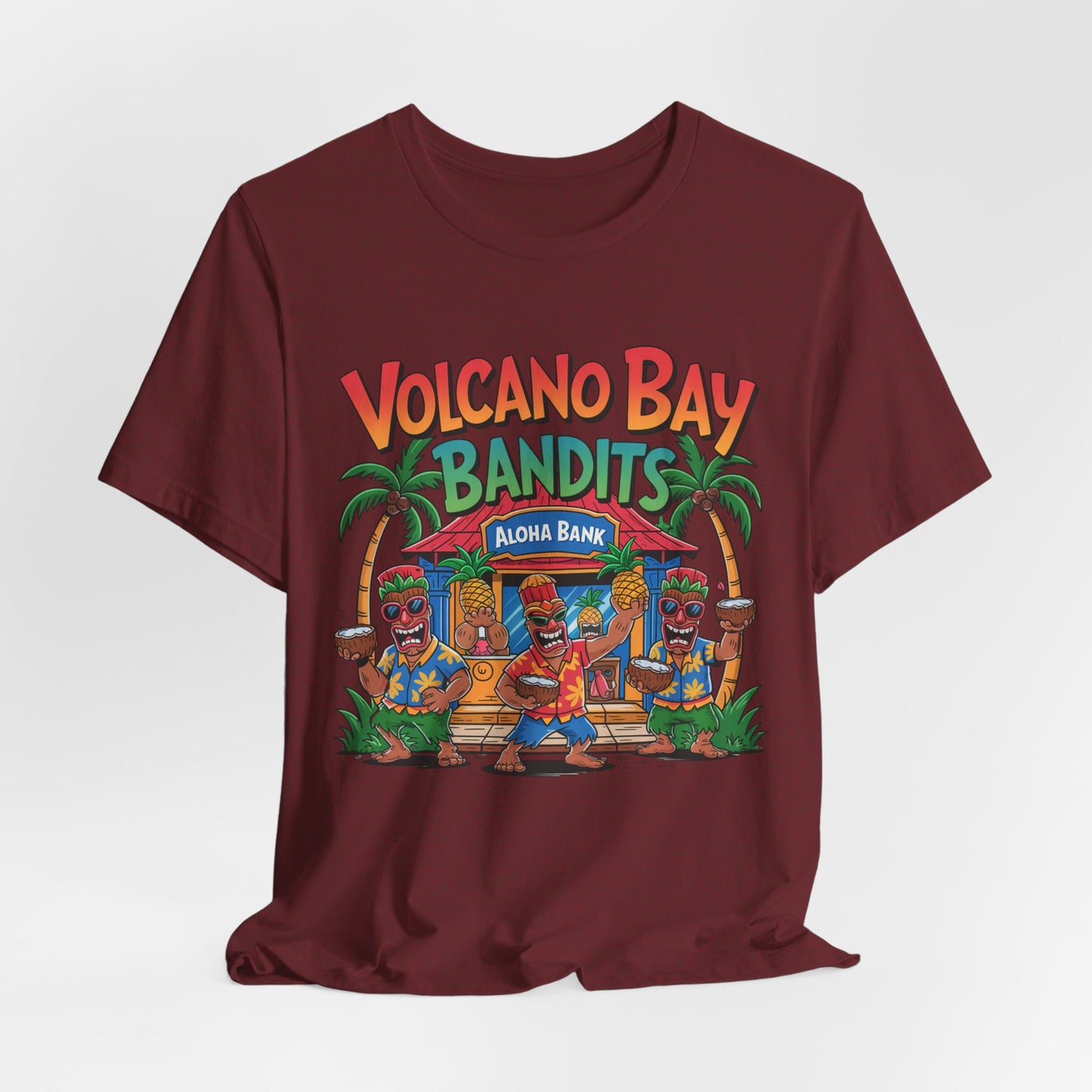 The Volcano Bay Bandits Graphic Tiki T-Shirt is a maroon unisex short sleeve shirt with dancing tiki characters, palm trees, and a hut featuring Aloha Bank—perfect for casual or adventure wear.