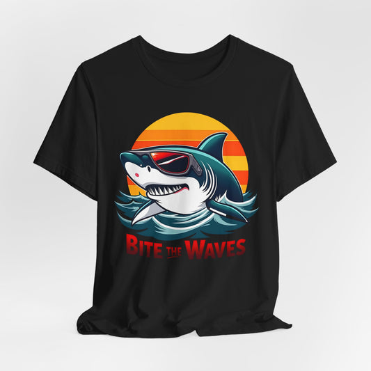 The Bite the Waves Shark T-Shirt is a black unisex jersey featuring a cartoon shark in sunglasses, emerging from water with a sunset. Bite the Waves appears in bold red letters, making it perfect for beach vacations.