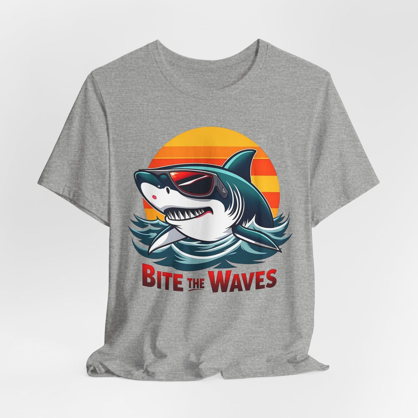 The Bite the Waves Shark T-Shirt is a gray unisex jersey featuring a cartoon shark in sunglasses, sunset backdrop, and bold red Bite the Waves text—perfect for adding playful style to your summer beach wardrobe.