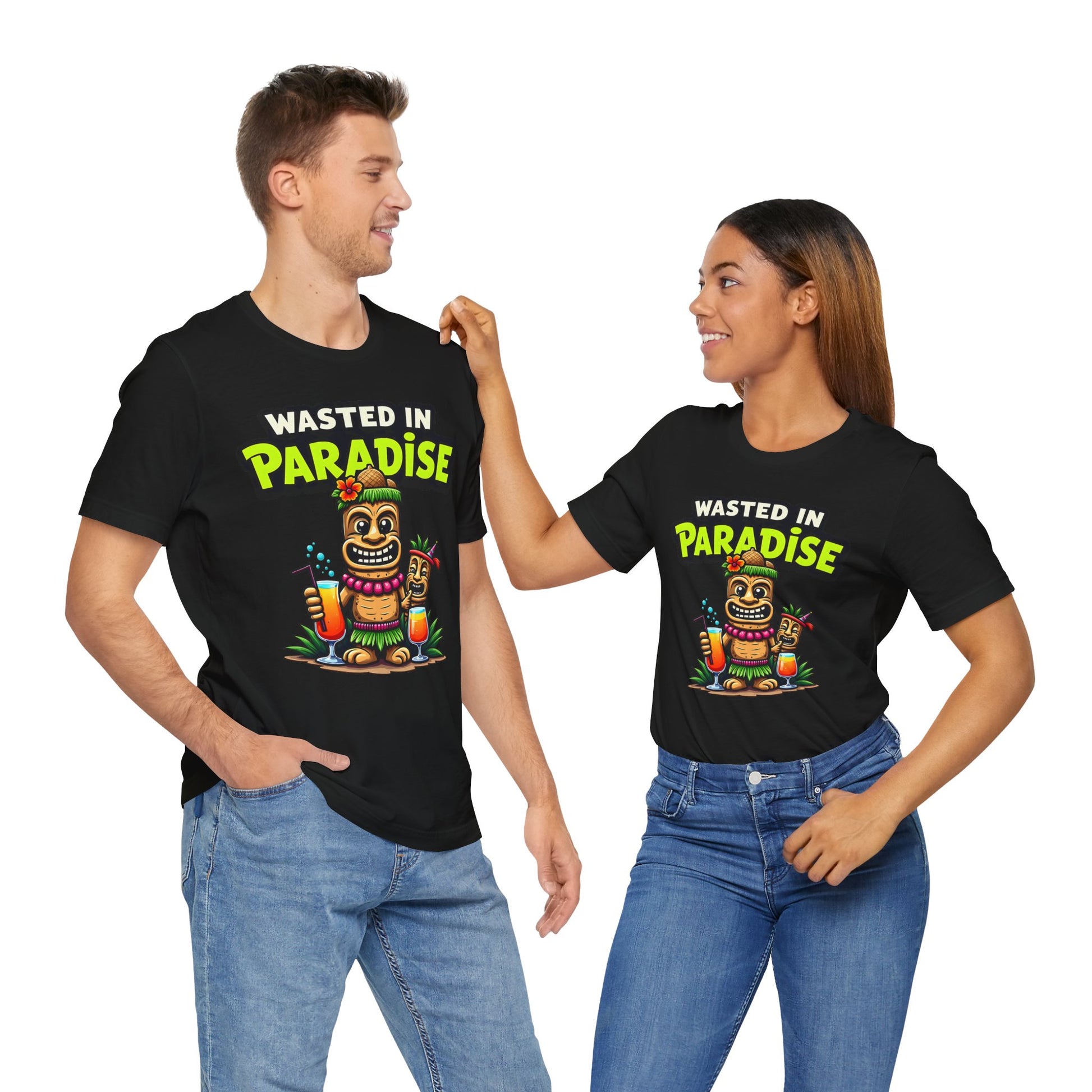 A man and woman smile at each other in matching Wasted in Paradise Graphic Tiki T-Shirts—unisex jersey tees featuring a vibrant tiki print and slogan, perfect for beach lovers’ vacation wardrobes. Both pair their black shirts with jeans for a relaxed vibe.