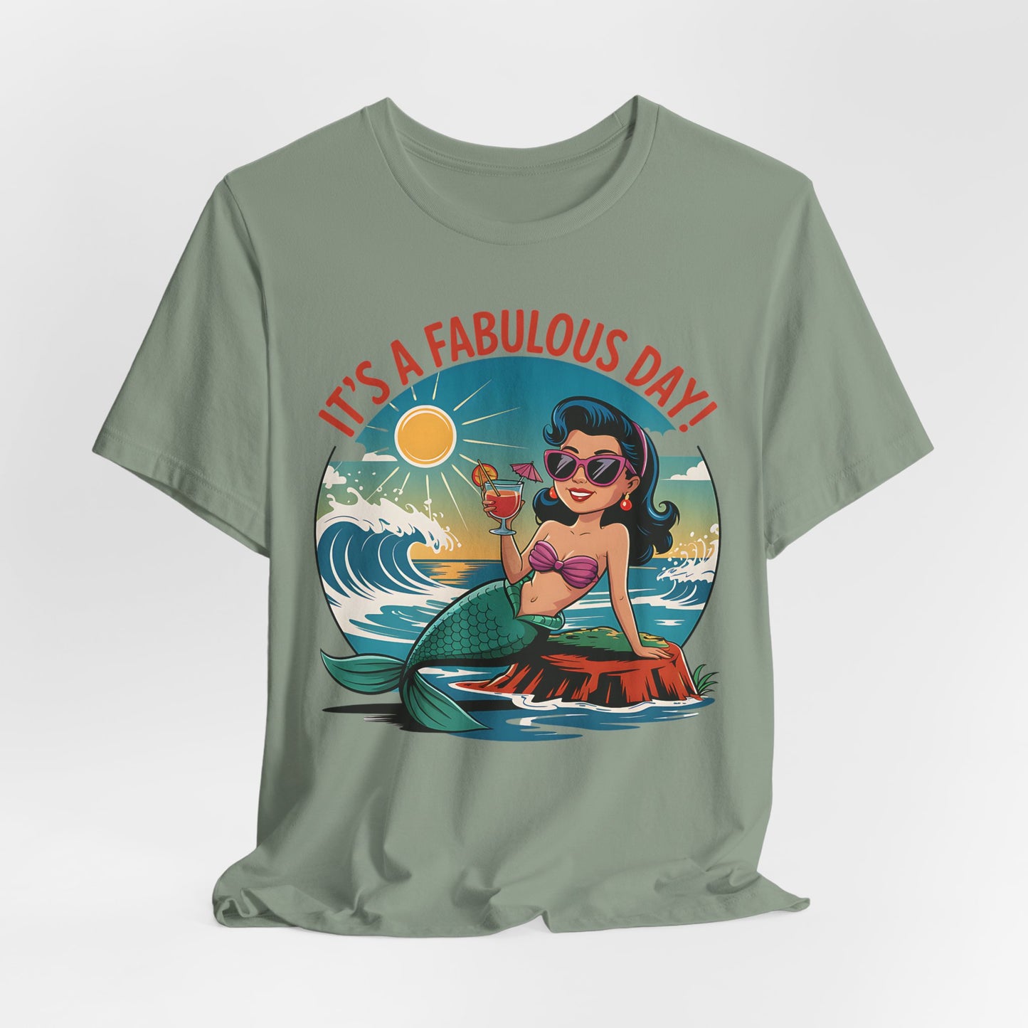 The Fabulous Day Mermaid Unisex Tee is a green jersey featuring a cartoon mermaid with dark hair, sunglasses, and pink shell bra on a rock enjoying ice cream. “IT’S A FABULOUS DAY!” text appears above with waves and sun in the background.