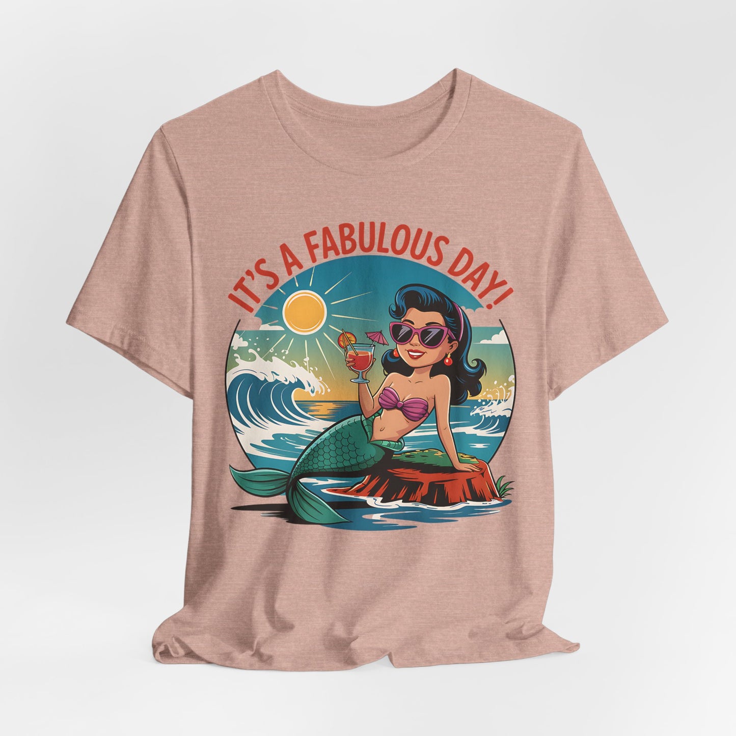 The Fabulous Day Mermaid Unisex Tee features a pink jersey with a retro mermaid graphic—she smiles in sunglasses, holding a drink on a rock by the waves under the sun, with ITS A FABULOUS DAY! above. Perfect for fantasy-themed events.