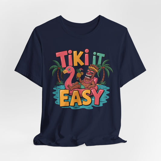 The Tiki It Easy Unisex Short Sleeve Tiki T-Shirt brings tropical beach vibes with a playful tiki statue on a pink flamingo float, palm trees, and bold Tiki It Easy lettering for a fun Hawaiian-themed look.
